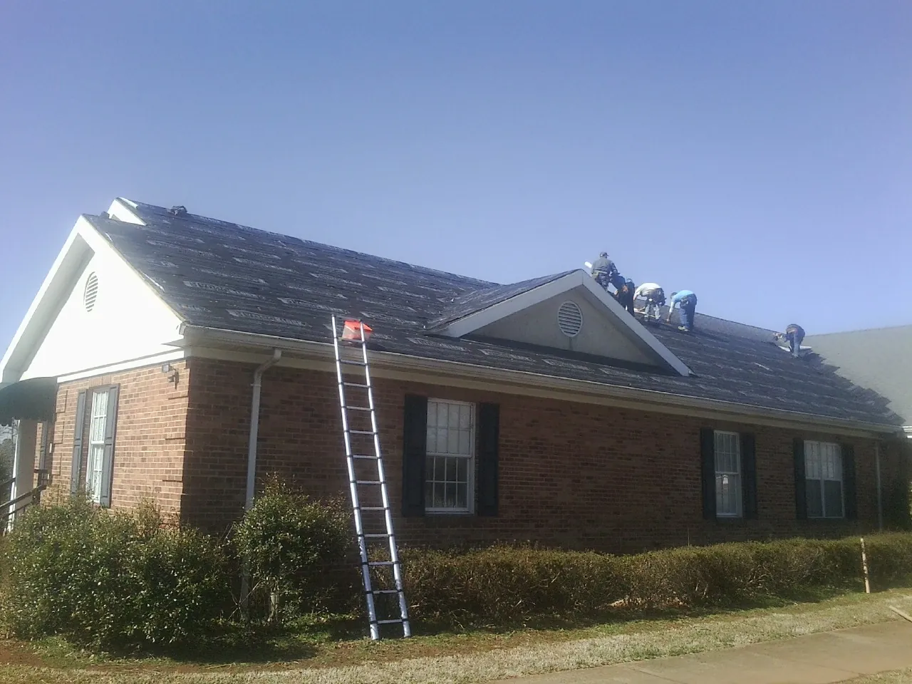 Crew tearing shingles off a brick ranch roof with a ladder set — Metal Roof Repair work by our crew in Wood Ridge