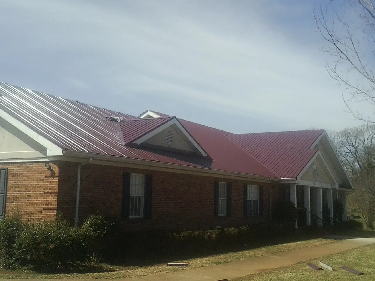 Red metal roof with gabled entries on a long brick building, from a Hail Damage Roof Repair job in Wood Ridge