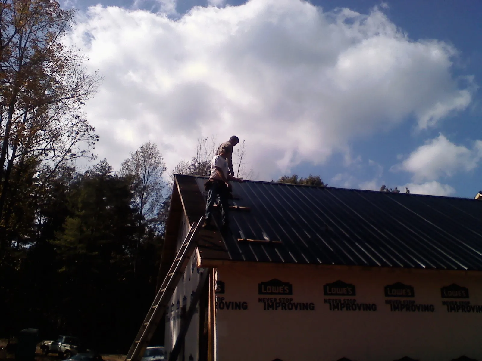 Roofer fastening dark metal panels high against a cloudy sky, from a Roof Inspection job in Wood Ridge