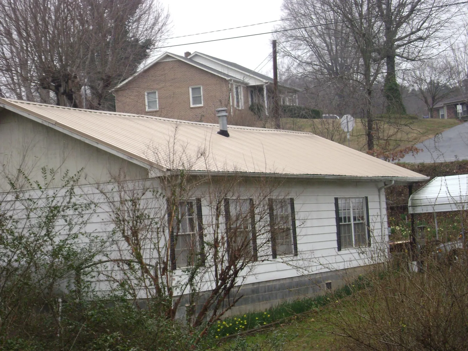 Tan metal roof on a white sided house set into a hillside — Commercial Roofing by Roofing Brothers in Wood Ridge